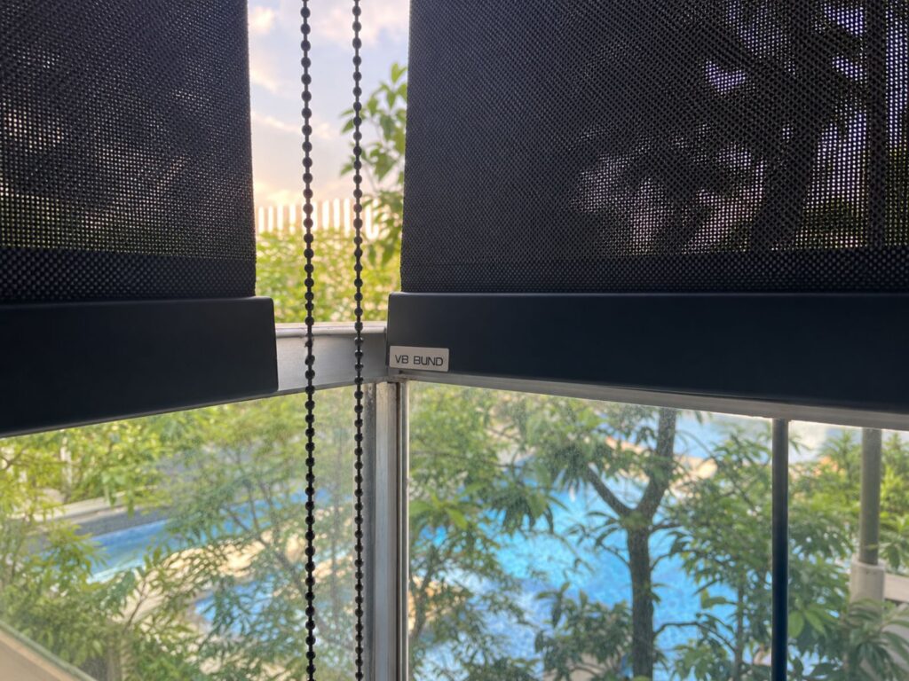 VB Blind outdoor roller blinds with black flat bottom bars, mesh fabric and manual pulley chains installed at an outdoor balcony area.